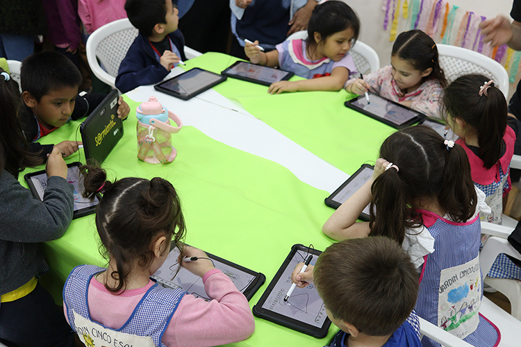 Una mesa con niños alrededor interactuando entre sí y sus tablets